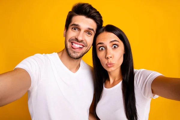 Foto de duas pessoas em humor tolo tomar selfies furar a língua fazendo rostos usar roupas casuais isolado cor amarela fundo — Fotografia de Stock