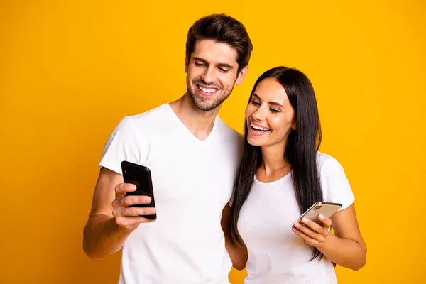 Photo de deux personnes tenant des téléphones regardant une vidéo humoristique drôle porter des vêtements décontractés isolé fond de couleur jaune — Photo