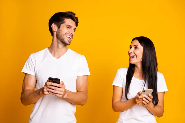 Photo de deux personnes tenant des téléphones vérifiant feednews rire de bonne blague porter des vêtements décontractés isolé couleur jaune fond — Photo