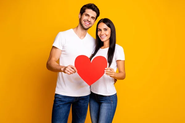 Foto de casal agradável abraço segurando em mãos grande papel coração confiar uns nos outros usar roupas casuais isolado cor amarela fundo — Fotografia de Stock