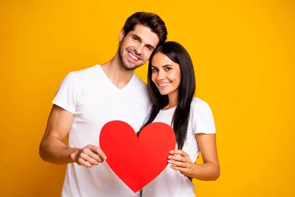 Foto von netten Paar umarmen halten in den Händen großes Papier Herz vertrauen einander tragen lässige Kleidung isoliert gelbe Farbe Hintergrund — Stockfoto