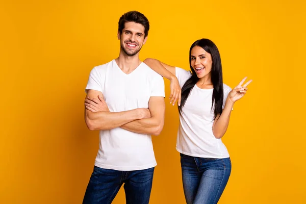 Foto de casal incrível trabalhando juntos melhor equipe mostrando v-sinal símbolo desgaste casual t-shirts e jeans isolado cor amarela fundo — Fotografia de Stock