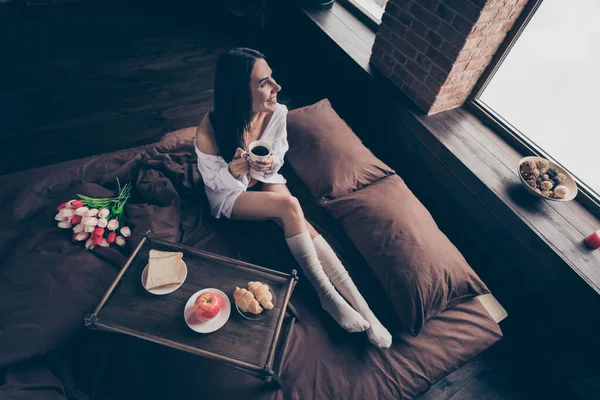 아름다운 명랑 한 꿈의 소녀가 침대에 앉아 커피 산업용 벽돌 로지 은 현대식 인테리어 주택을 마시며 놀랄 만한 조화 로운 삶을 즐기고 있는 높은 각도로 바라본 위 — 스톡 사진
