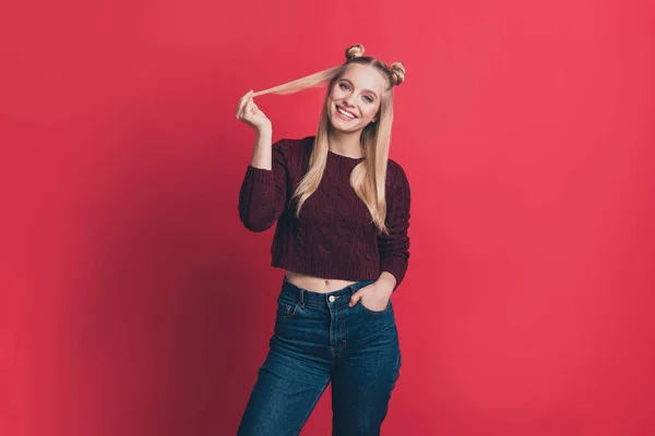 Foto von erstaunlichen Millennial Lady hält Hände in Taschen positive Stimmung spielen mit langen Locken tragen Strickpullover und Jeans isoliert pastellrote Farbe Hintergrund — Stockfoto
