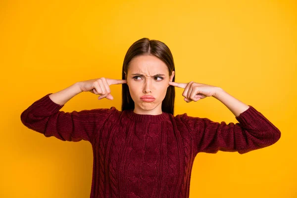 Portrait of sullen lady closing her ear not to hear noise wearing burgundy jumper isolated over yellow background