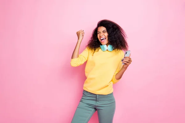 Retrato de loco funky hipster africano chica uso celular obtener retroalimentación de seguidores levantar puños grito sí celebrar logro desgaste amarillo suéter pantalones aislados sobre rosa color de fondo — Foto de Stock