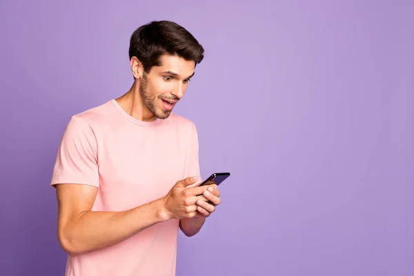 Profile side view portrait of his he nice attractive cheerful glad focused guy wearing pink tshirt holding in hands using digital device gadget isolated on violet purple lilac pastel color background — ストック写真