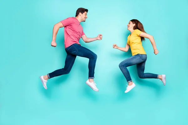 Full length body size side view of nice attractive active sporerful cheerful couple running jumping in air having fun isolated over bright vivid shine vibrant green turquoise background — стоковое фото