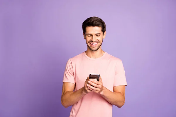 Portrait of his he nice attractive cheerful cheery guy wearing pink tshirt holding in hands using 5g app cell modern technology isolated over violet purple lilac pastel color background — ストック写真