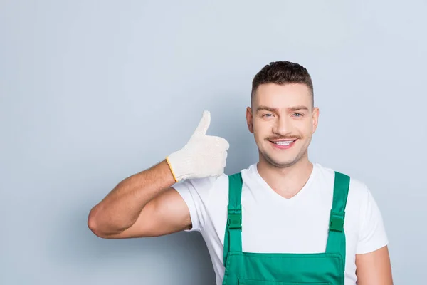 Foto de guapo viril músculos chico sosteniendo brazo levantando pulgar hacia arriba ingeniero experto aconsejando fresco servicio desgaste verde seguridad dungarees aislado gris fondo — Foto de Stock