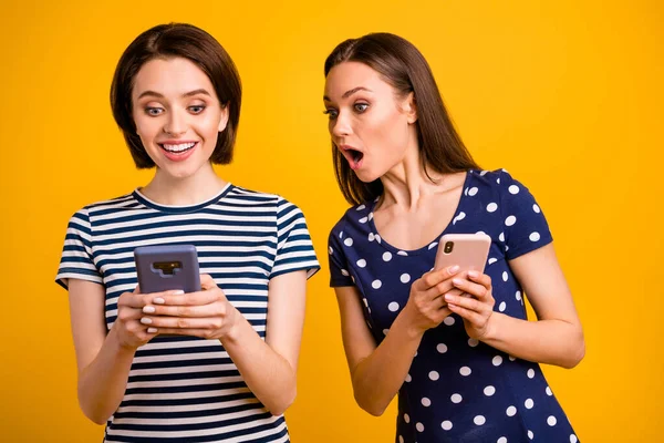 Фото двух симпатичных дам с телефонами, читающих хорошие новости не верю, что удача носить летом случайные модные футболки изолированный желтый фон — стоковое фото