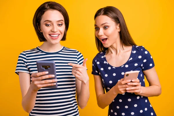 Фото двох красивих жінок, що тримають телефон прямим пальцем на екрані, показують хороші новини, не вірять, що удача носить випадкові модні футболки ізольовані жовтий фон — стокове фото