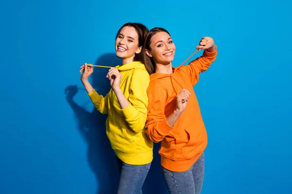 Profil foto av vackra två flickvänner dam stående back-to-back i bästa gott humör bär casual ljusa hoodies och jeans isolerade levande blå färg bakgrund — Stockfoto