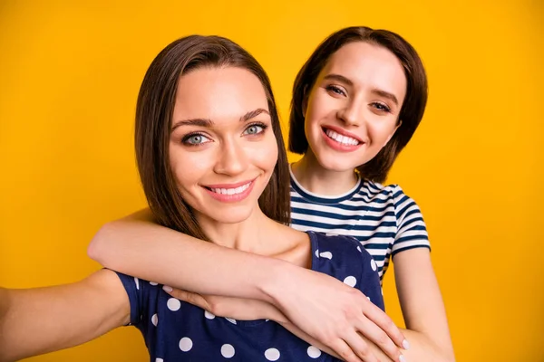 Close up photo of two amazing cute ladies making selfies hugging piggyback wear summer casual trendy t-shirt isolated yellow background — Stock fotografie