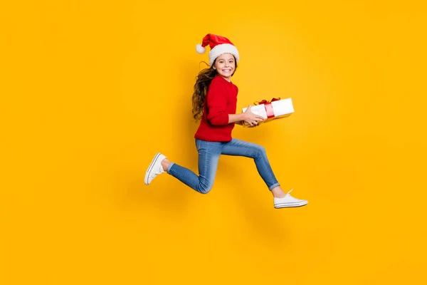 Foto de perfil em tamanho real de uma senhora louca pulando alto levando caixa de presente de santa em x-mas meia-noite desgaste vermelho pulôver de malha e jeans isolado fundo amarelo — Fotografia de Stock