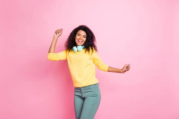 Retrato de positiva alegre funky africana chica danza en la vida nocturna club escuchar música tienen auriculares tienen divertido desgaste pantalones de suéter amarillo aislado sobre rosa color de fondo — Foto de Stock