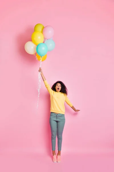 Κάθετη πλήρους μήκους φωτογραφία από έκπληκτη συναισθηματική αστεία έφηβος hipster κρατώντας πολλά μπαλόνια στο χέρι αίσθηση ότι μπορεί να ανατιναχθεί μέχρι τον ουρανό στα σύννεφα το καλοκαίρι ημέρα απομονωμένο παστέλ φόντο χρώμα — Φωτογραφία Αρχείου
