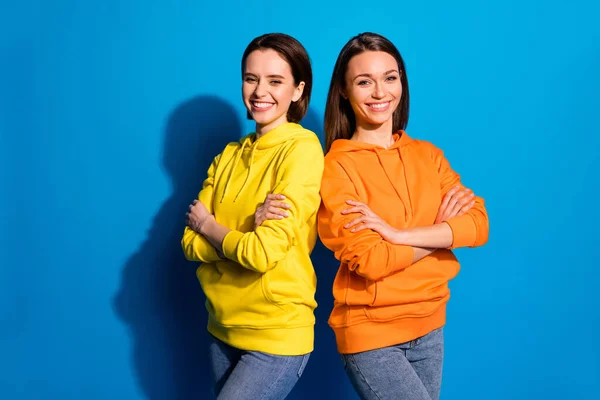 Zdjęcie ładnych dwóch dziewczyn pani stojących plecami do siebie w dobrym nastroju skrzyżowanie ramiona nosić casual jasne bluzy i dżinsy odizolowany niebieski kolor tła — Zdjęcie stockowe