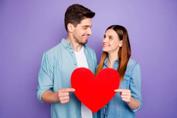 Retrato de románticos cónyuges encantadores estudiantes tienen tarjeta de papel rojo signo de corazón grande de su romance disfrutar de la fecha 14-febrero vacaciones usar jeans camisa aislada sobre el fondo de color violeta púrpura — Foto de Stock