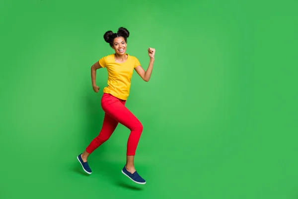 Foto de perfil de tamaño completo de la señora de piel bastante oscura saltando alta competición deportiva corredor participante usar casual amarillo camiseta pantalones rojos aislado fondo verde —  Fotos de Stock