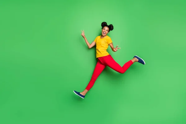 Full body foto van mooie donkere huid dame springen hoog lopende concurrentie deelnemer kwam eerst om te eindigen show v-tekens dragen gele t-shirt rode broek geïsoleerde groene achtergrond — Stockfoto