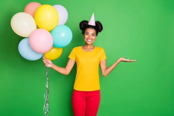 Foto di bella signora pelle scura in possesso di molti palloncini d'aria e di nuovo prezzo di vendita prodotto che offre agli acquirenti credito usura casual giallo t-shirt pantaloni rossi e cappuccio di carta isolato sfondo verde — Foto Stock