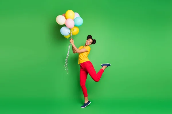 Full length photo of pretty millennial dark skin lady holding air balloons going to fly up in sky wear casual κίτρινο t-shirt κόκκινο παντελόνι απομονωμένο πράσινο φόντο — Φωτογραφία Αρχείου