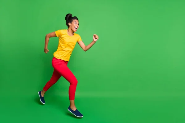 Full size profile photo of pretty dark skin lady jumping high sports competition jogging participant wear casual yellow t-shirt red pants isolated green background