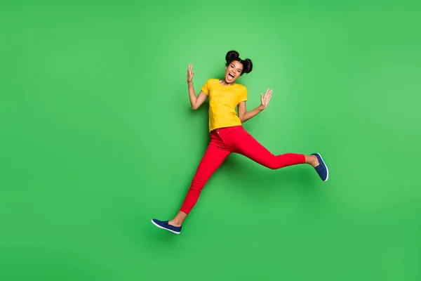 Фотографія повної довжини досить темної шкіри леді стрибає високі спортивні змагання бігун учасник одягнений в повсякденну жовту футболку червоні штани ізольовані зелений фон — стокове фото