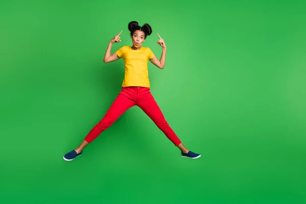 Pełny rozmiar zdjęcie dość ciemna skóra pani skoków wysoki wskazując palce na nowe stylowe fryzury nosić casual żółty t-shirt czerwone spodnie odizolowane zielone tło — Zdjęcie stockowe