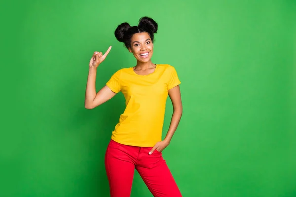 Фото дивовижної темної шкіри леді, що вказує пальці на стильне волосся, порадивши відвідати прохолодний салон волосся майстер одягати повсякденну жовту футболку і червоні штани ізольовані зелений фон — стокове фото