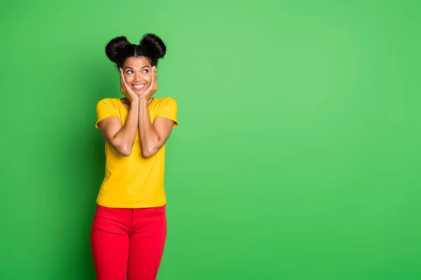 Photo of pretty dark skin lady holding arms on cheeks having best weekend mood looking empty space interested wear casual yellow t-shirt piros nadrág elszigetelt zöld háttér — Stock Fotó