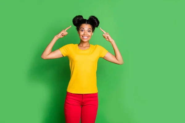 Photo of amazing dark skin lady indicating fingers on stylish hairdo advising visit cool salon hair master wear casual yellow t-shirt and red pants isolated green background — Stock Photo, Image