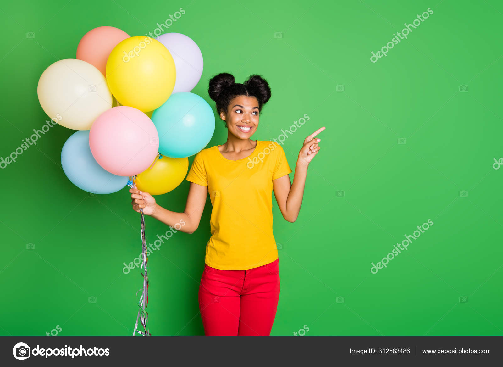 Photo of pretty dark skin lady holding many air balloons directing finger  empty space on sale prices wear casual yellow t-shirt red pants isolated  green background Stock Photo by ©deagreez1 312583486
