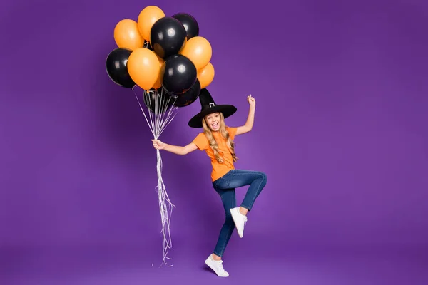 Full size photo of little witch lady halloween party holding many air balloons excited to start cool chill wear orange t-shirt wizard hat isolated purple color background — Φωτογραφία Αρχείου