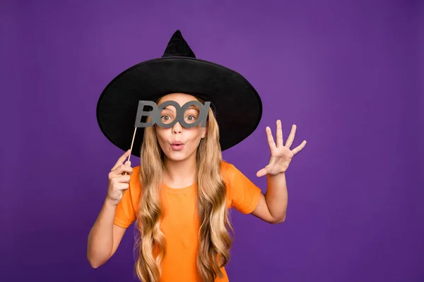 Boo. Foto de pequena bruxa jogar encantador papel halloween partido segurando papel vara olhar assustador desgaste laranja t-shirt chapéu de assistente isolado cor roxa fundo — Fotografia de Stock