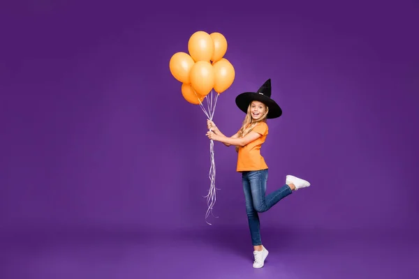 Foto em tamanho completo da pequena bruxa senhora festa de Halloween segurando muitos balões de ar animado desgaste de refrigeração laranja t-shirt chapéu de assistente isolado cor roxa fundo — Fotografia de Stock