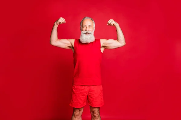 Retrato de Santa Claus musculoso alegre mostrando sus bíceps sonriendo usando ropa deportiva de moda roja aislada sobre fondo rojo — Foto de Stock