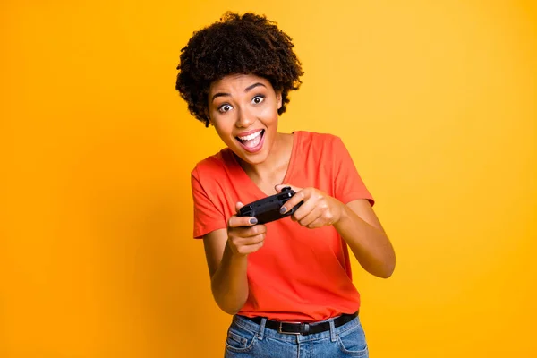 Foto van vrolijke charmante schattige lieve aantrekkelijke speler genieten spel proces houden joystick met haar handen dragen oranje t-shirt jeans denim geïsoleerde heldere kleur achtergrond — Stockfoto