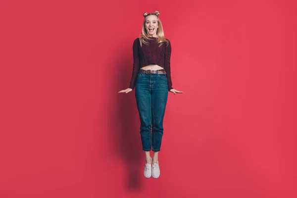 Full längd foto av roliga attraktiv dam hoppar hög glädje i flygning slitage stickade vinrött pullover och jeans isolerade pastell röd färg bakgrund — Stockfoto