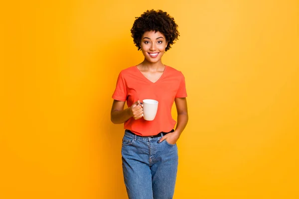 노란색 선명 한 색상 배경으로 고립되어 있는 동안 데님 진을 입고 커피 한잔을 들고 있는 매력적 이고 매력적 인 흑인 여자 친구의 사진 — 스톡 사진