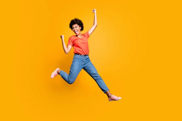 Foto de tamaño completo de la señora loca funky encantado salto celebrar la victoria en la lotería levantar los puños grito sí usar camiseta roja jeans zapatillas aisladas sobre fondo de color amarillo —  Fotos de Stock