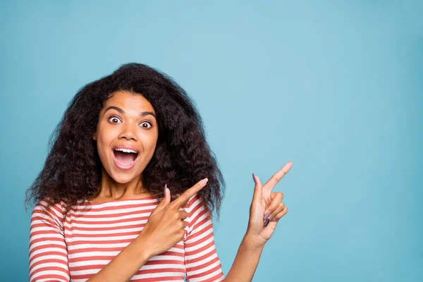 Foto de excitada mujer dulce negra alegre y extática apuntando al espacio vacío con los dedos delanteros gritando regocijándose aislados sobre el fondo azul vivo de color —  Fotos de Stock