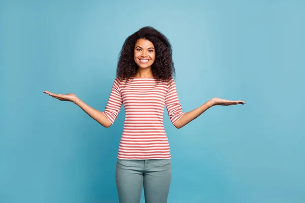 Photo of pretty sales manager dark skin lady holding new low prices products on open arms wear casual striped sweater isolated pastel blue color background — Stock Photo, Image