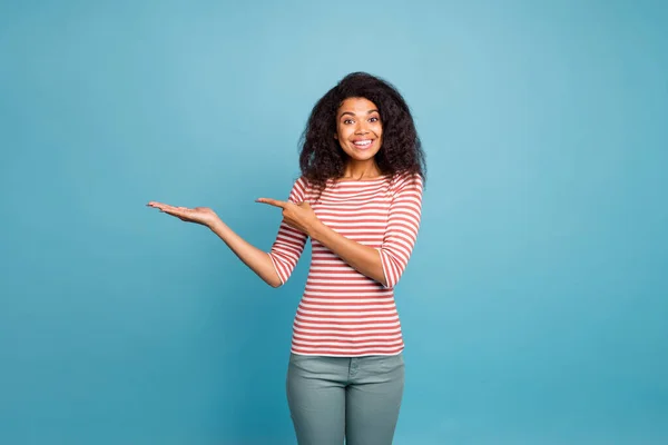 Photo of cheerful excited ecstatic crazy cheerful nice cute sweet pretty black girlfriend pointing at empty space on her palm smiling toothily wearing grey trousers pants isolated over blue vivid — Stock Photo, Image
