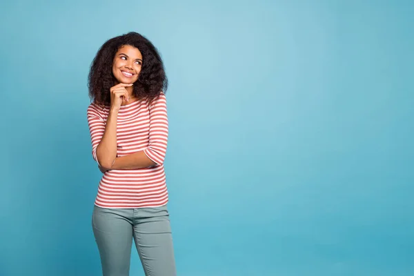 Foto mempesona wanita kulit hitam cantik yang manis mengenakan celana abu-abu menonton ruang kosong menyentuh dagu dengan tangan terisolasi warna biru latar hidup — Stok Foto