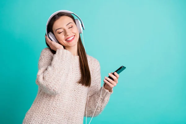 Retrato de chica alegre positiva hipster escuchar pistas de sonido favoritas en su teléfono celular disfrutar de usar auriculares digitales de punto suéter de lana aislado sobre fondo de color turquesa verde azulado — Foto de Stock