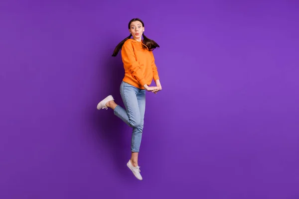 Foto de longitud completa de la divertida chica joven funky salto se siente despreocupado infantil en movimiento desgaste moderno ropa adolescente vaqueros zapatillas blancas aisladas sobre violeta color púrpura fondo —  Fotos de Stock