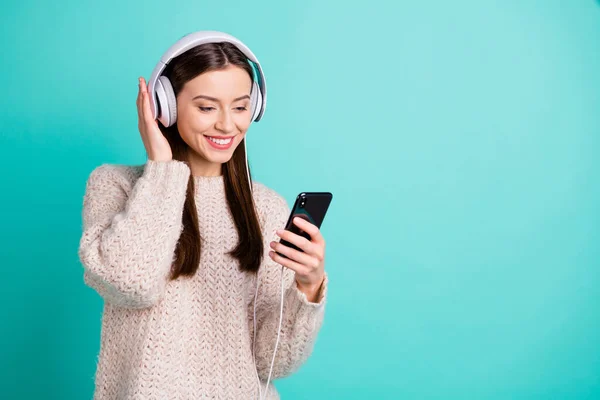 Foto convertida de encantadora chica positiva en auriculares escuchar pistas de sonido elegir melodía en su teléfono móvil usar jersey de lana blanca aislado sobre fondo de color turquesa verde azulado — Foto de Stock