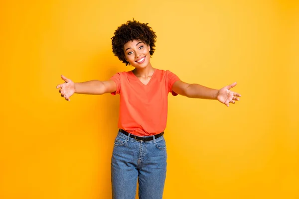 Photo of cheerful charming trendy cute black lady inviting you to hug with her wearing jeans denim orange t-shirt kind and lovely isolated over yellow vivid color background — Stock Photo, Image